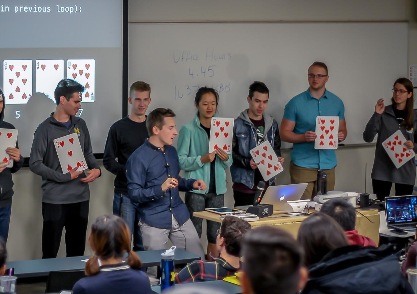 Maxim teaching a class as students hold up large playing cards to demonstrate a sorting algorithm